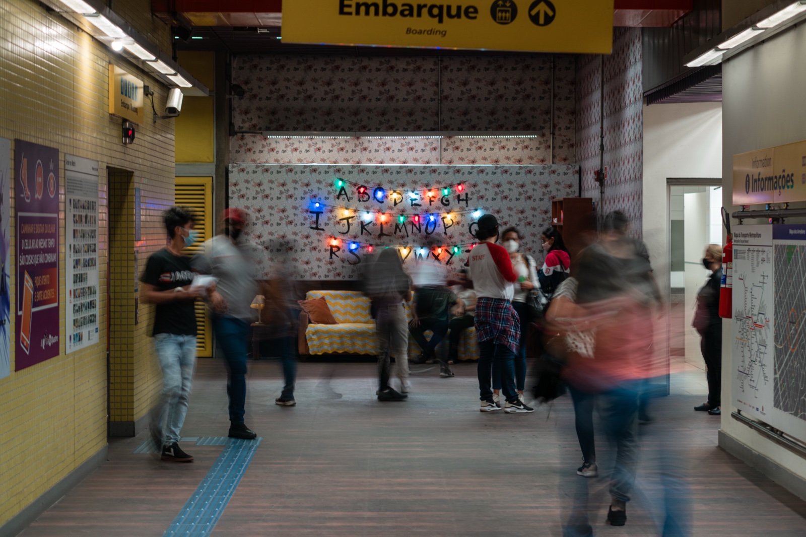 Commuters riding the station escalator down past the show artwork applied to the walls