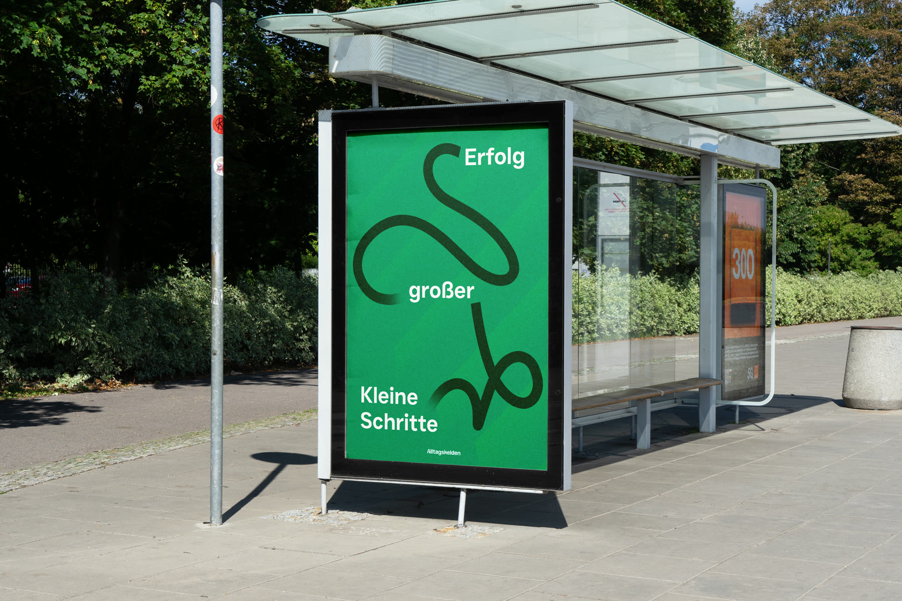 Green poster at a bus stop, carrying the brand's line drawing and the words Kleine Schritte großer Erfolg, small steps great success