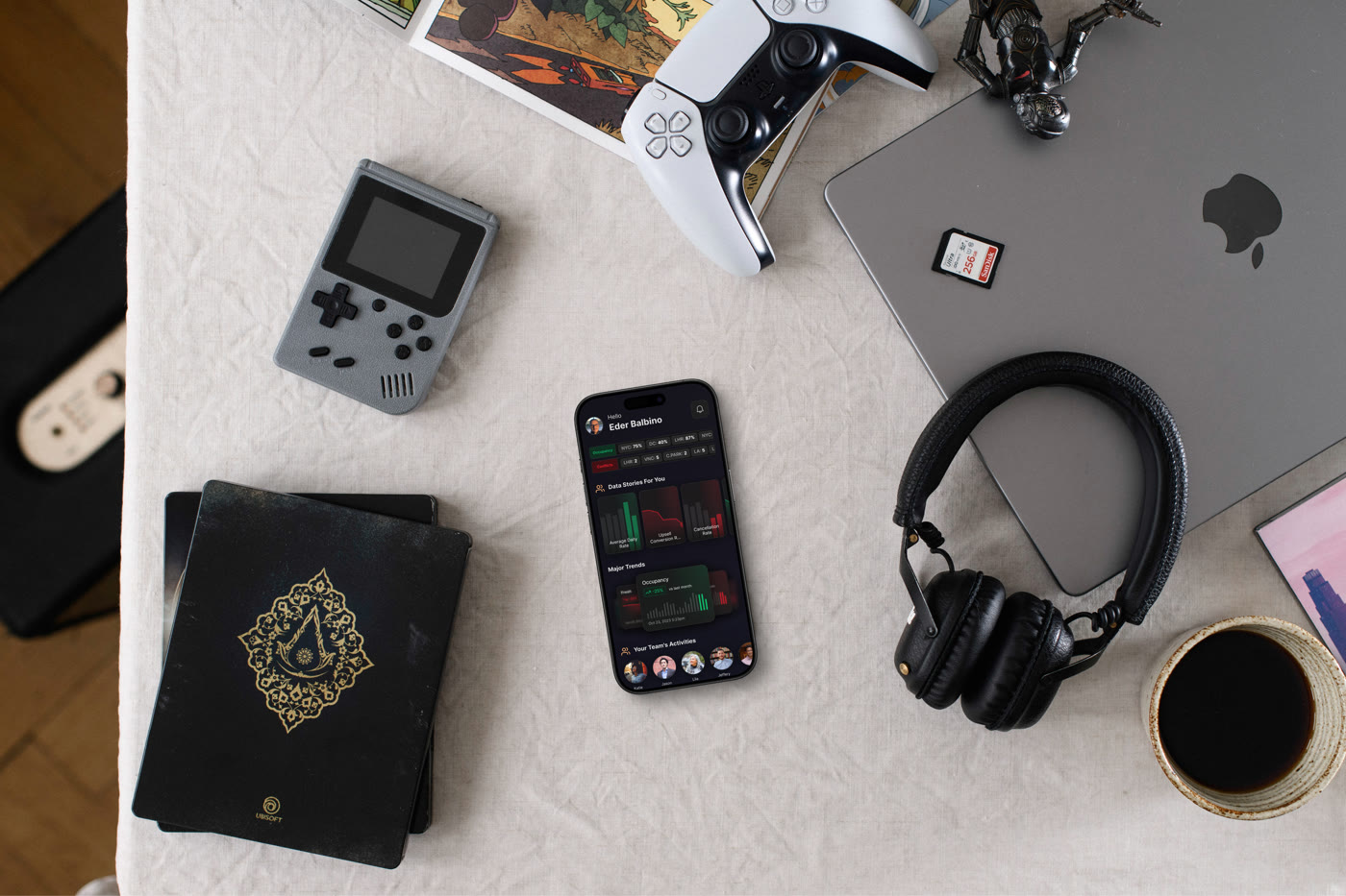 Overhead view of a desk with a phone showing the Gaio app, its data stories, major trends and team activity, among headphones, a game controller and a cup of coffee