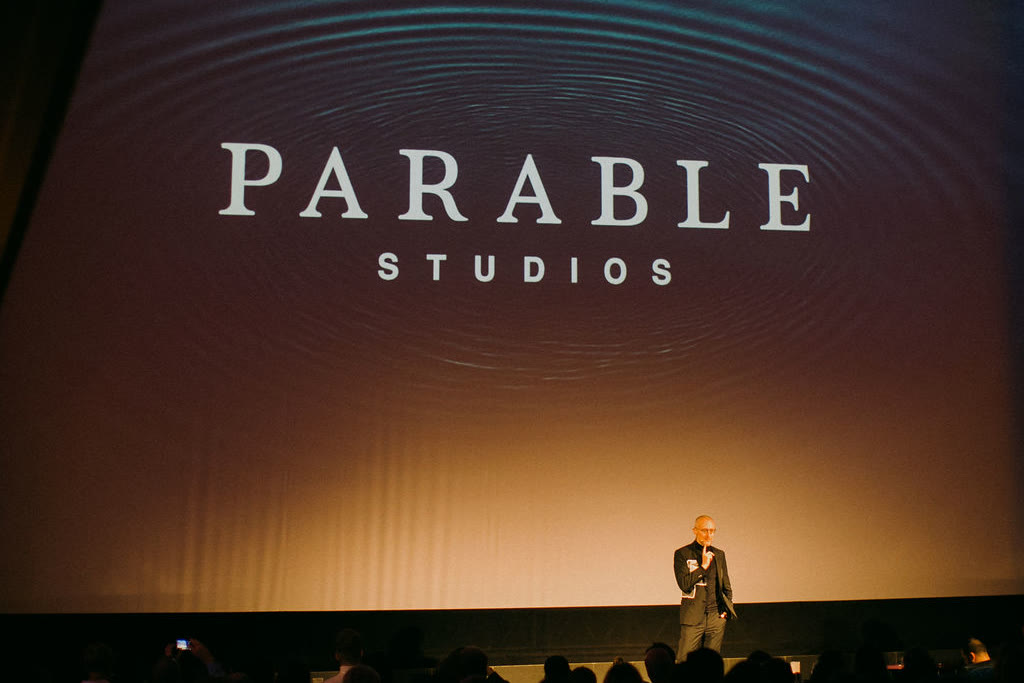 The Parable Studios logotype projected on the cinema screen, above the stage where one of the founders speaks to the audience at the debut