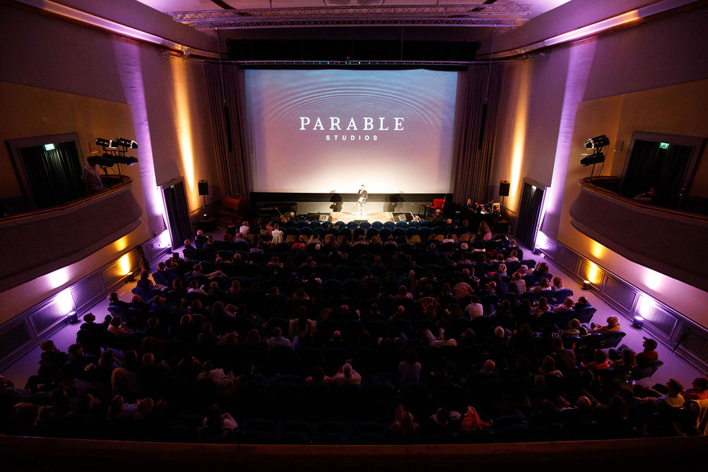 The full auditorium at Kino Babylon seen from the back of the room, the Parable Studios mark on screen and the walls lit in purple
