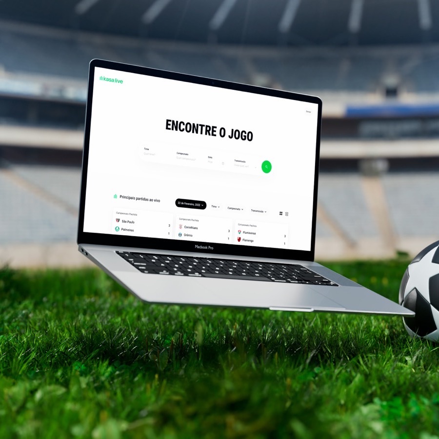 Open laptop on a stadium pitch showing the kasa.live match search, with a football beside it